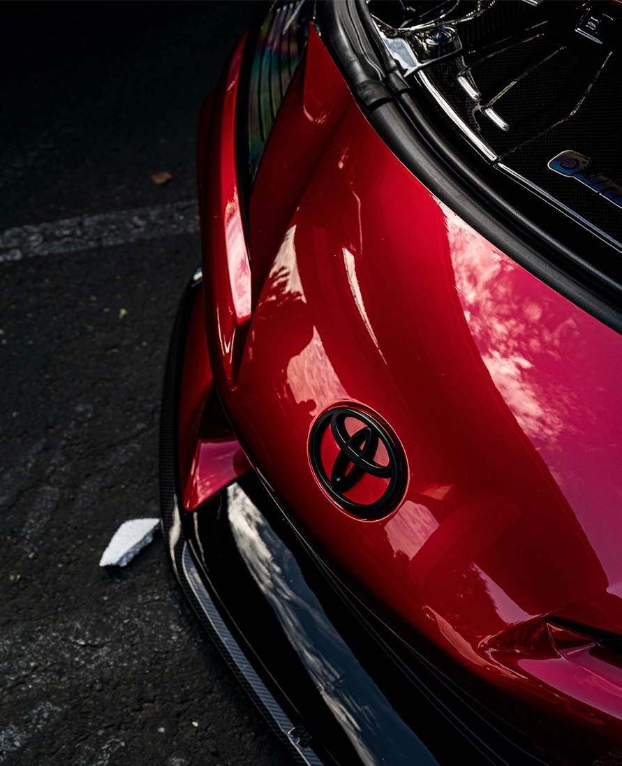 Tight crop on the rear quarter panel of a red car showing a circular emblem