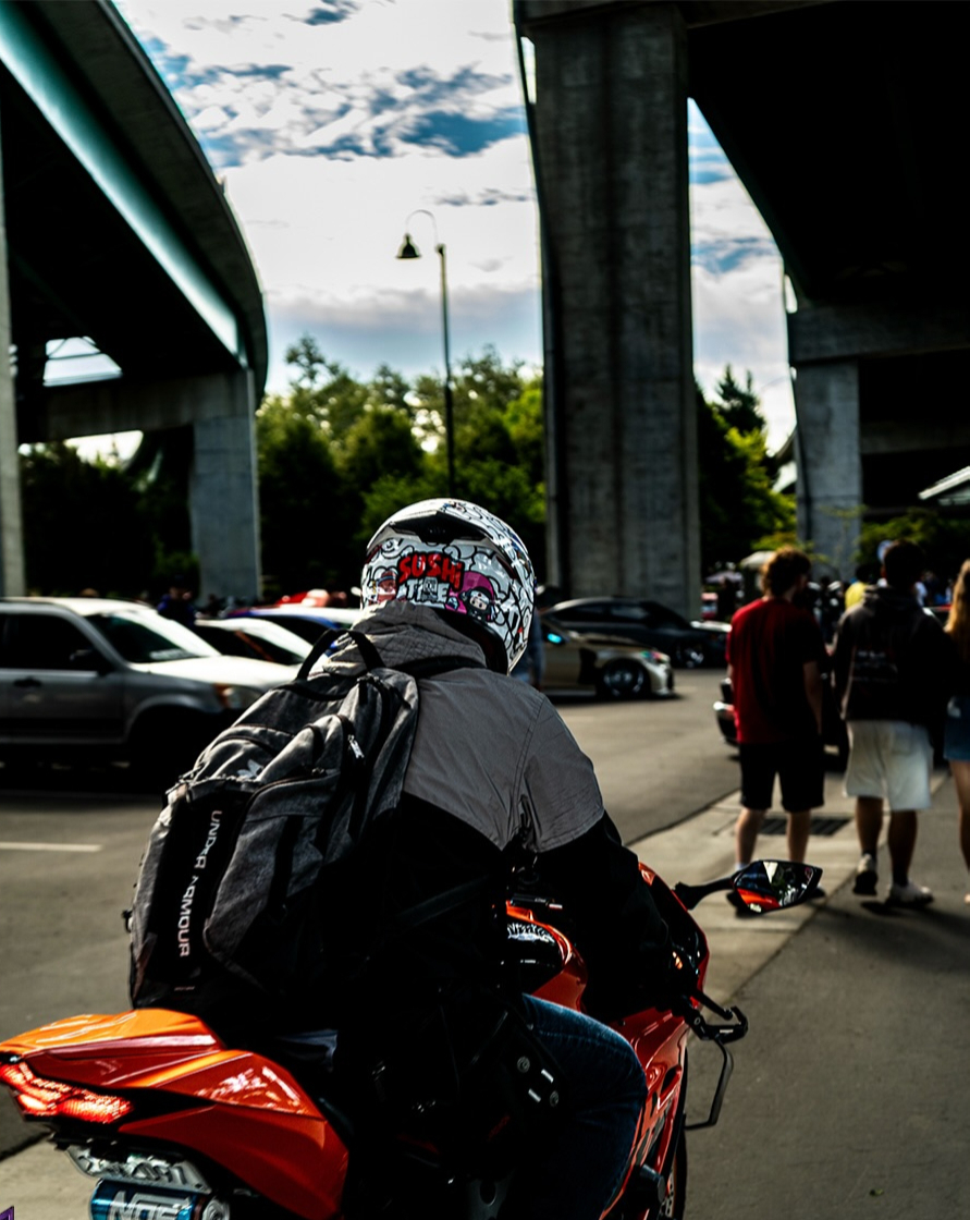 Rider in a helmet and leathers seated on a motorcycle with a crowd and parked cars behind