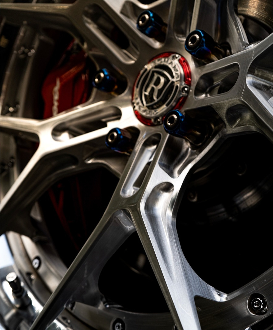 Close up of a polished forged wheel with blue titanium hardware