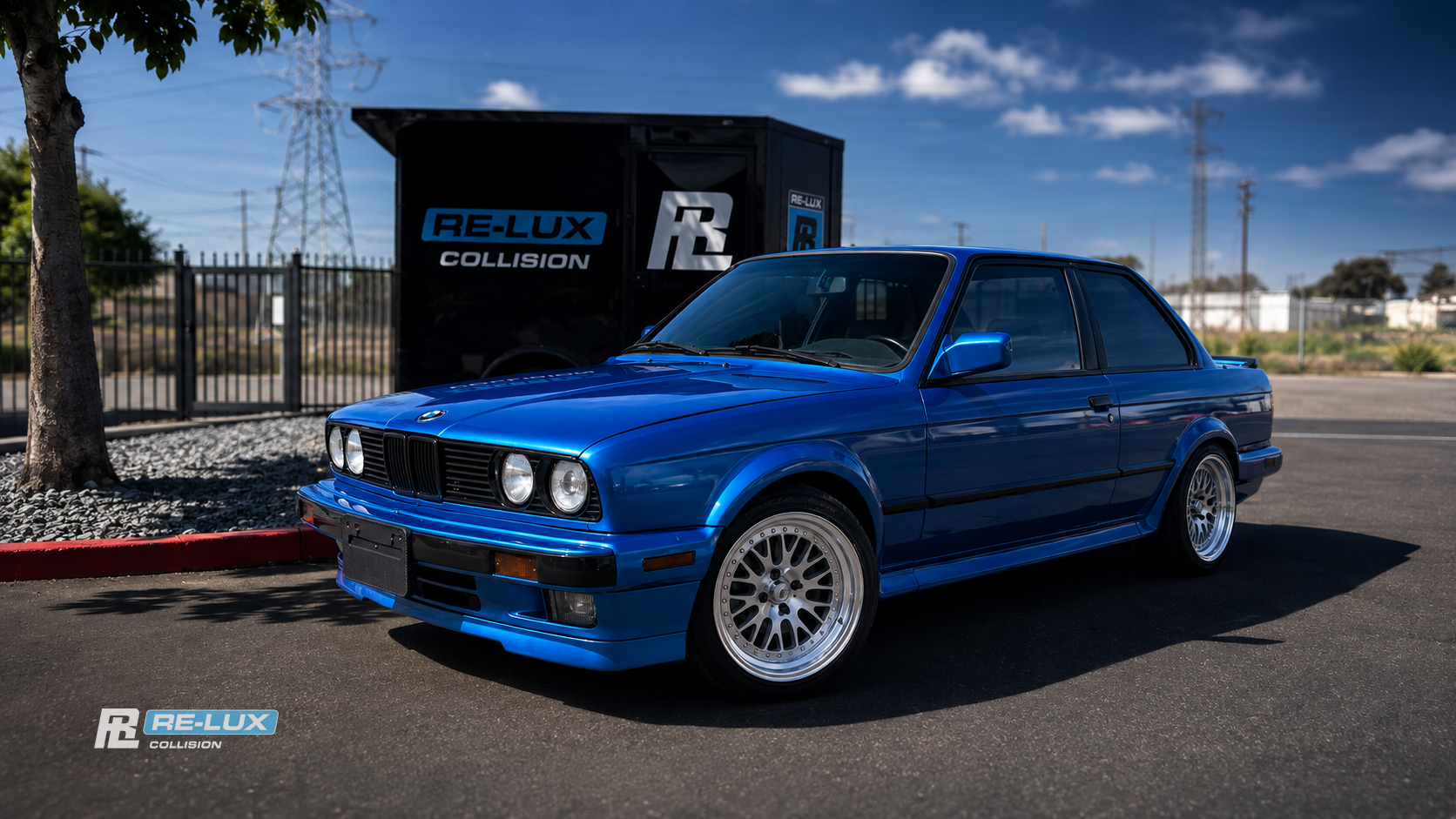Blue BMW 3 Series, front quarter, parked in front of the Re-Lux Collision sign