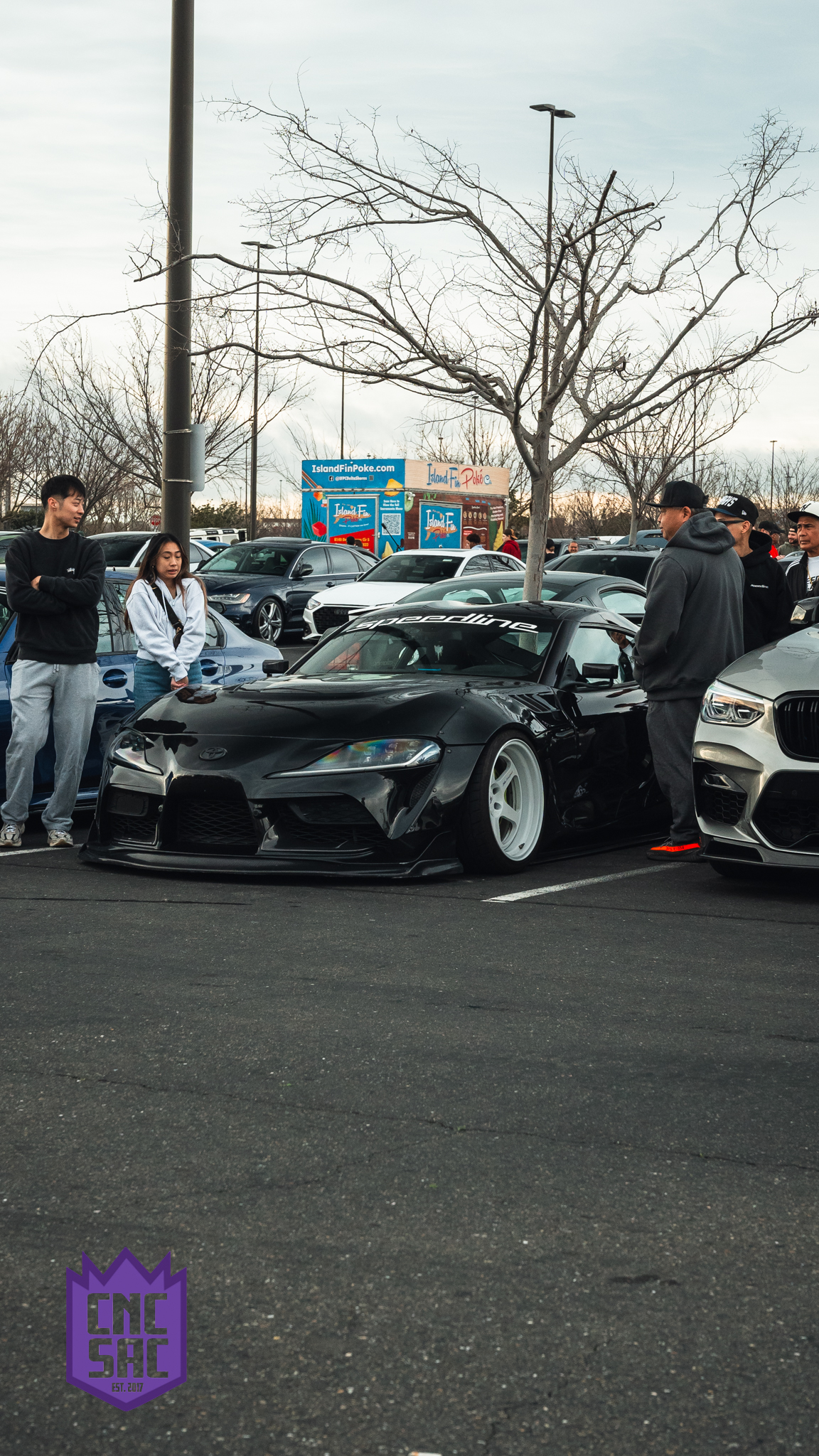 A black widebody coupe with attendees alongside it