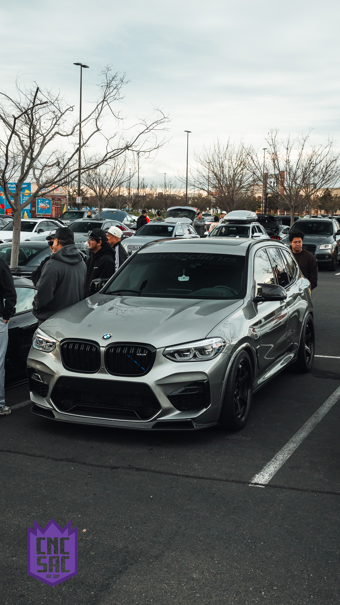 Grey BMW X3 M, front three quarter, in a packed parking lot