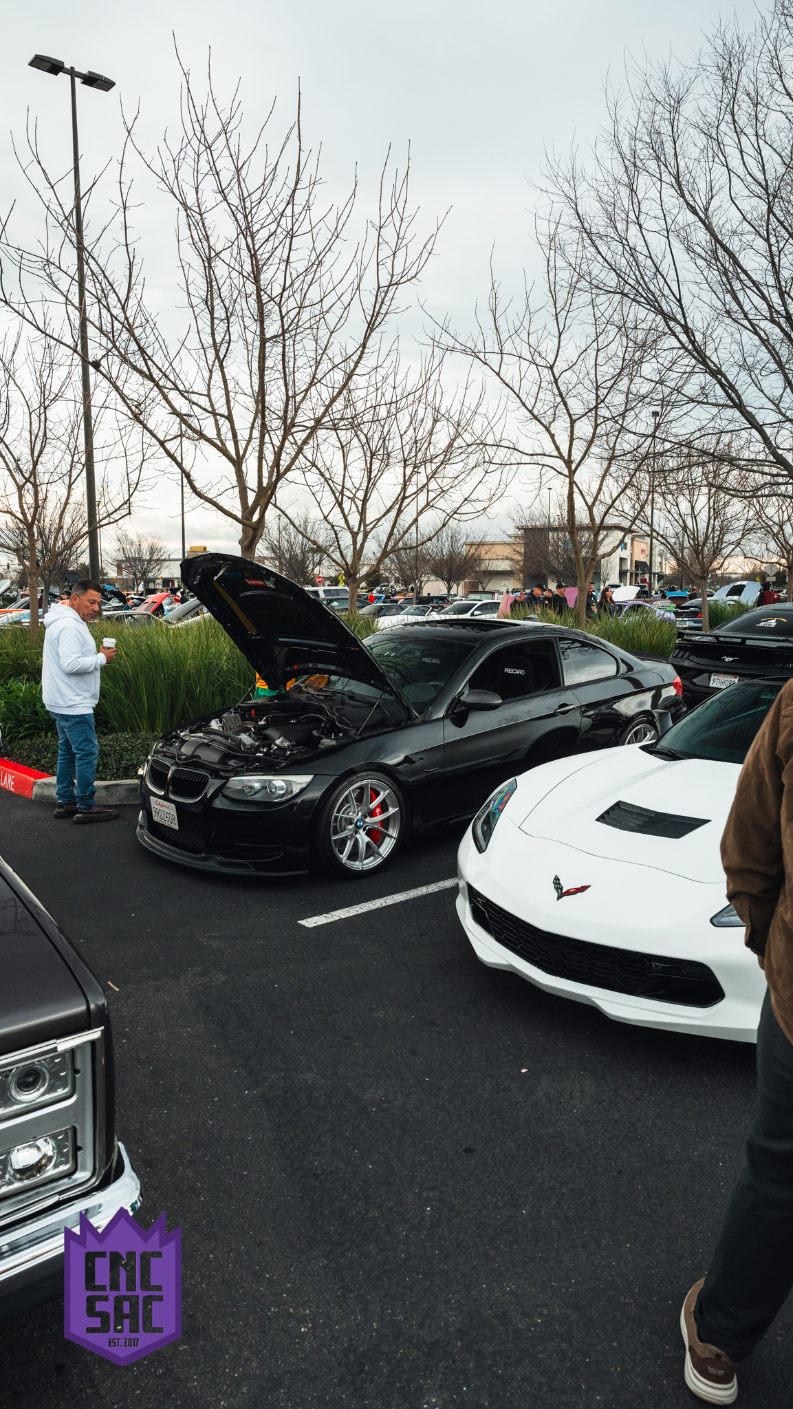 Attendees looking under the raised hood of a car at a Cars and Coffee Sac event