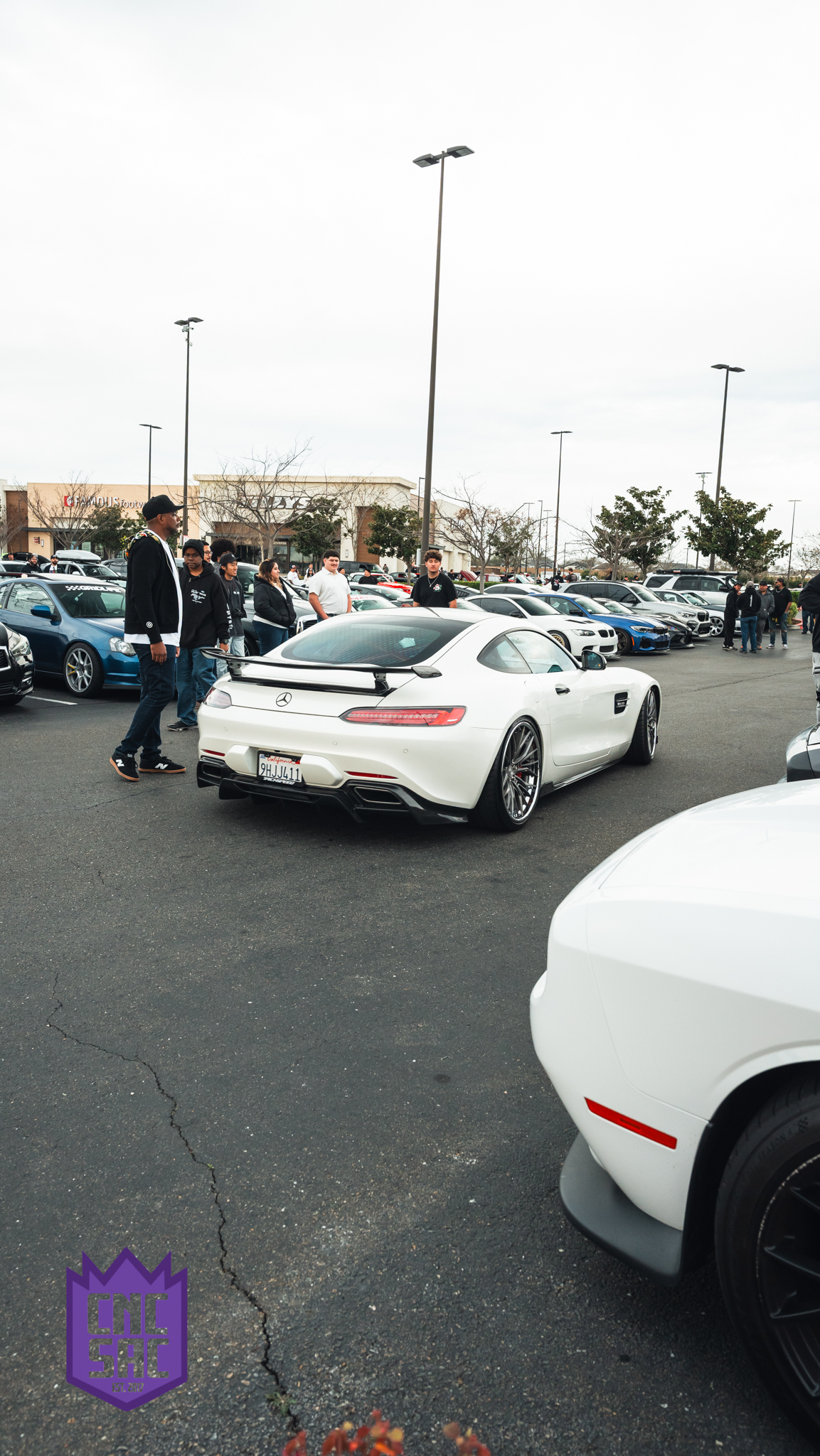 A white coupe with a rear wing, attendees walking past