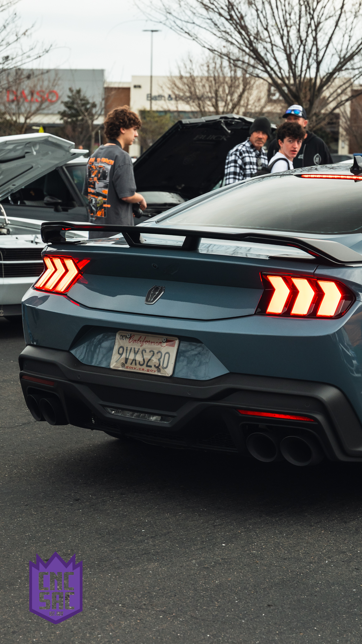 Attendees around a dark Ford Mustang at a Cars and Coffee Sac event