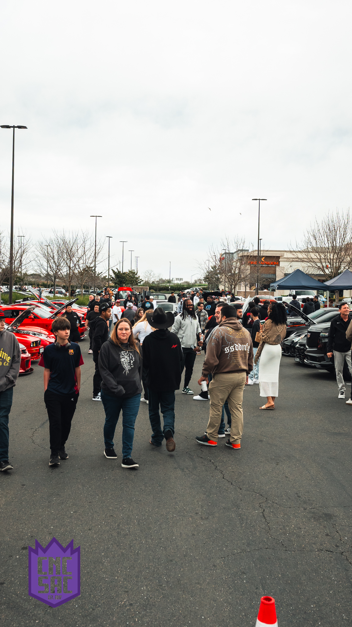 A crowd of attendees and cars filling the lot at a Cars and Coffee Sac event