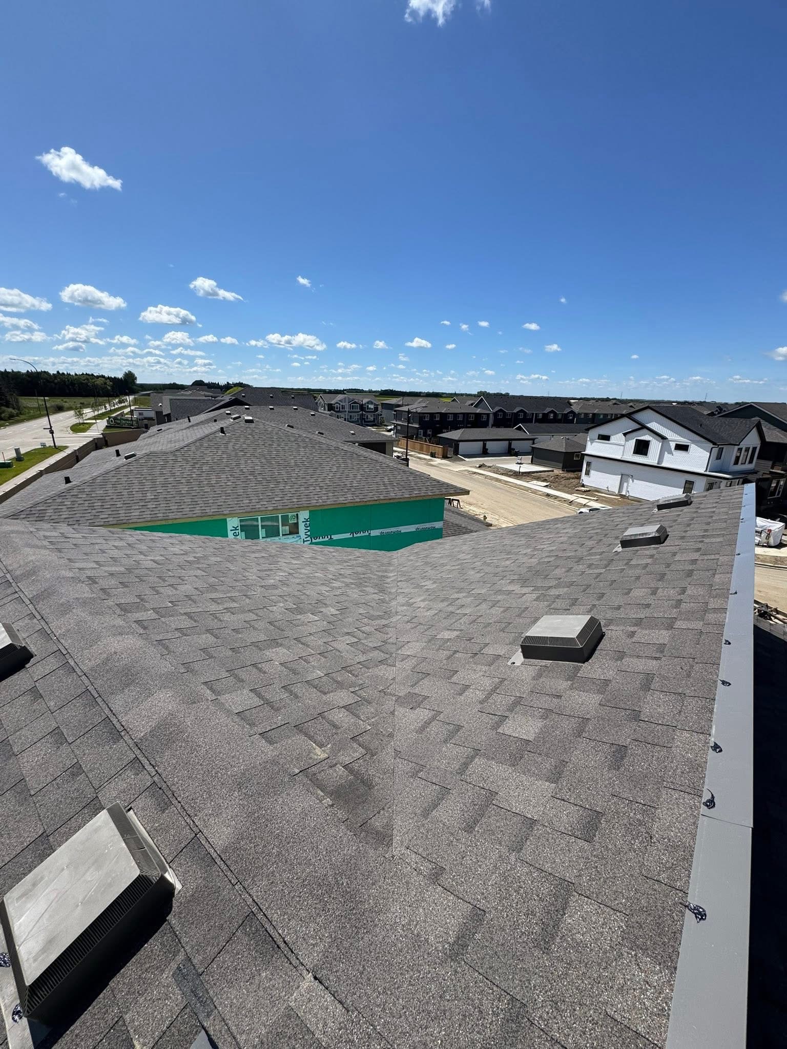 Residential roof with gray shingles and neighboring homes under a blue sky