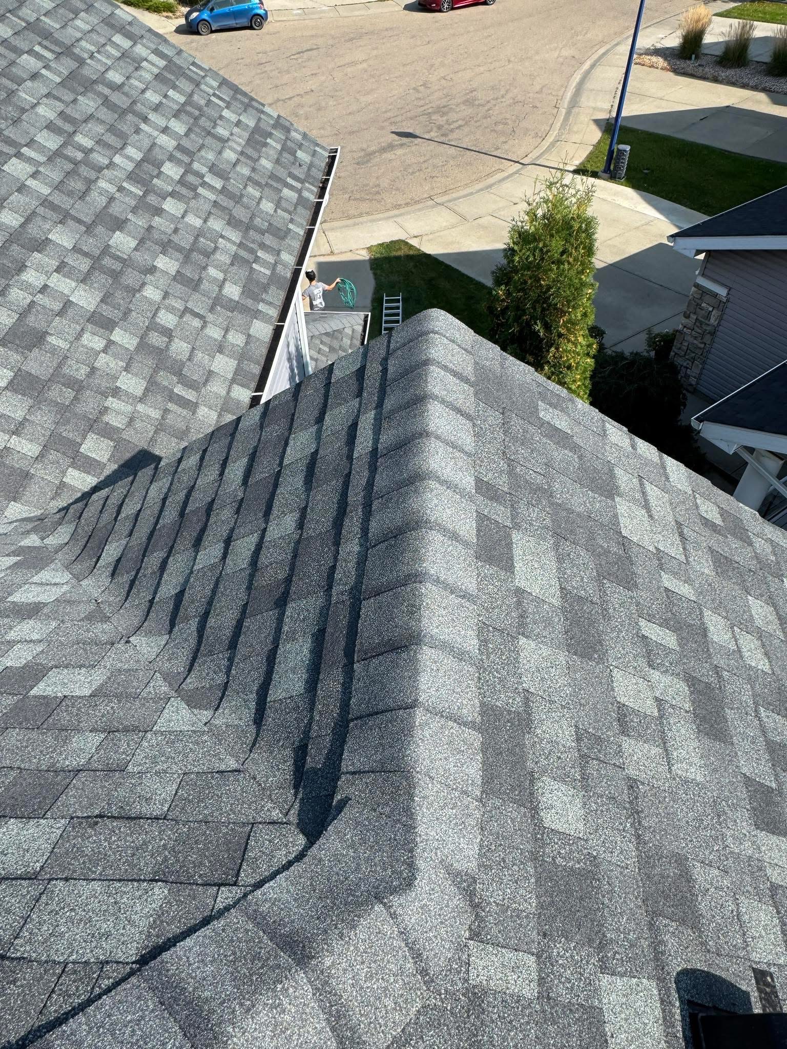 A roofer uses a hose on a residential roof while checking water drainage
