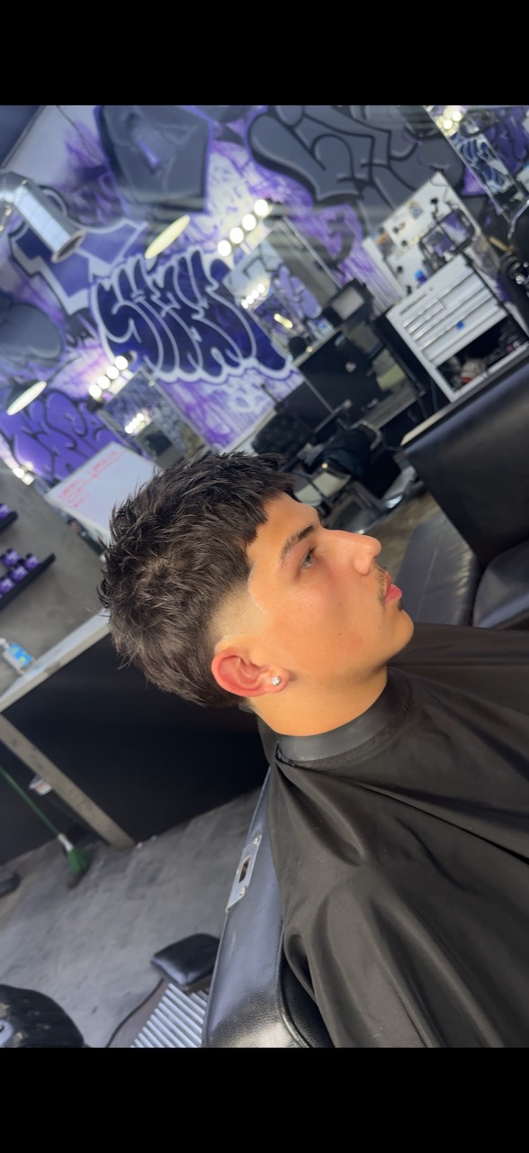 Client in profile with a short textured cut against the shop’s purple mural.