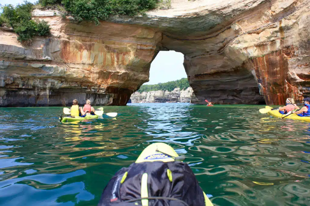 Paddling Michigan kayak tours - a group of kayakers in tandem sea kayaks paddling close to the colorful Pictured Rocks cliffs