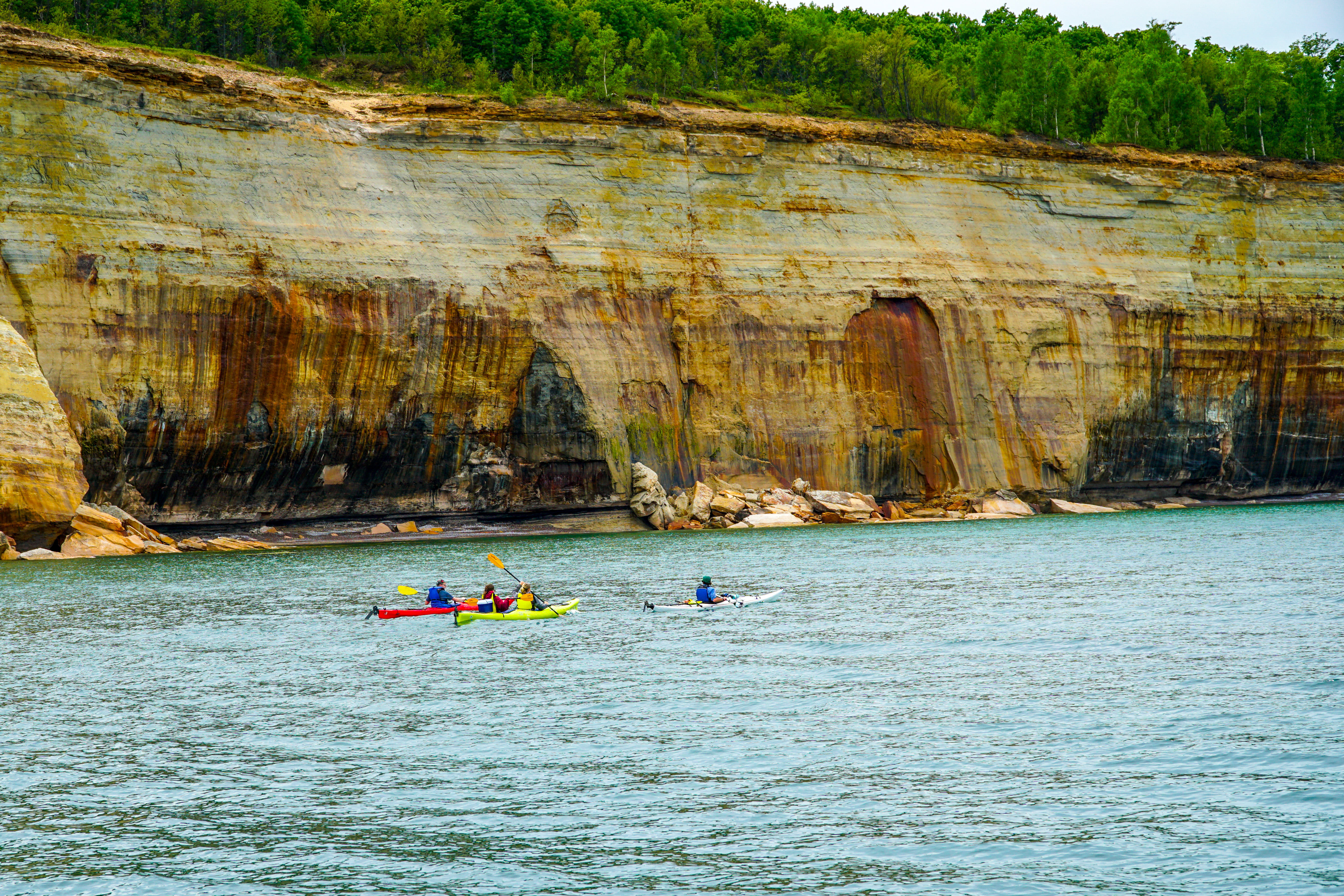 Kayakers paddling beneath the massive, colorful sandstone cliffs - one of the best Pictured Rocks kayak tours on Lake Superior