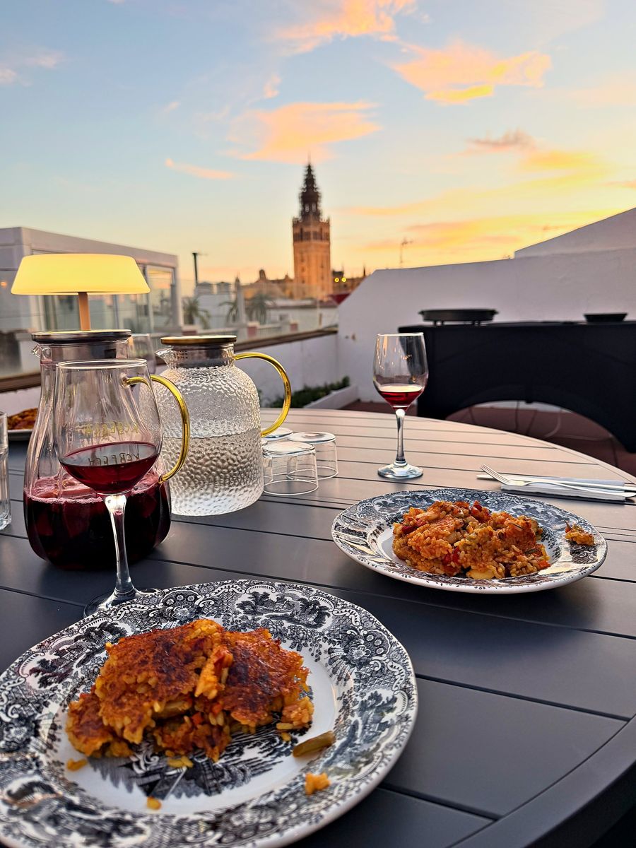 Paella served with sangria on the rooftop table as the sun sets behind the Giralda, Seville