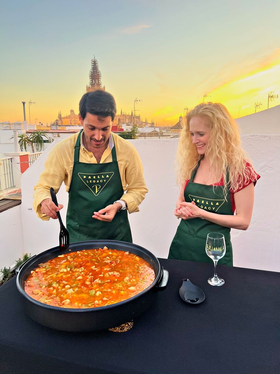 Guests stir their paella as the sun sets behind the Giralda on the Paella Legacy rooftop