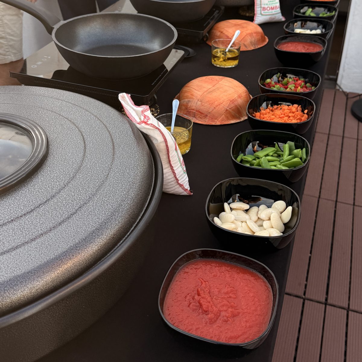 A paella class station on the Paella Legacy rooftop: grated tomato, garrofón and flat green beans, diced peppers and carrot, olive oil and a bag of bomba rice, ready to cook