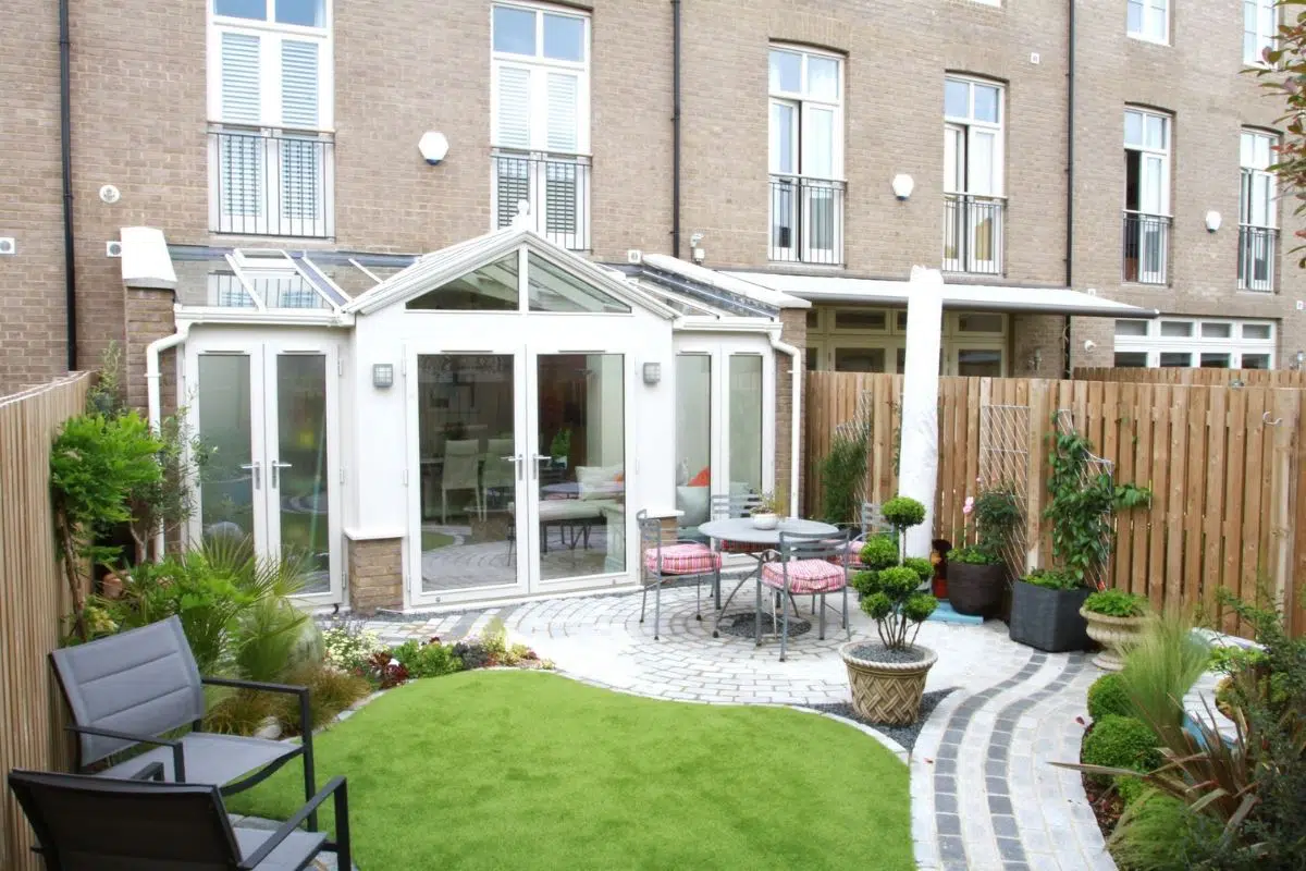 Interior view of a glass extension with a landscaped garden, featuring a round table with chairs, potted plants, and a seating area, showcasing a modern design suitable for conservatories in Surrey.