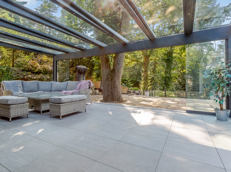 Modern modular extension featuring a glass roof, comfortable seating area with cushions, surrounded by greenery and natural light, showcasing premium design and a seamless connection to the outdoor environment.