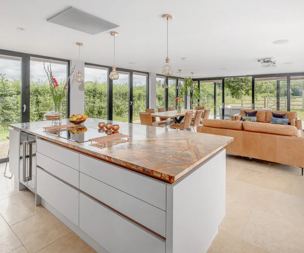 Bespoke conservatory by Room Outside featuring large windows, a glass roof, and a cozy seating area, surrounded by greenery.
