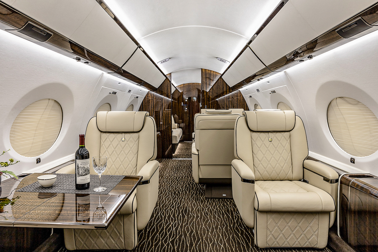 Custom private jet interior with light brown leather seating and fine wood trim