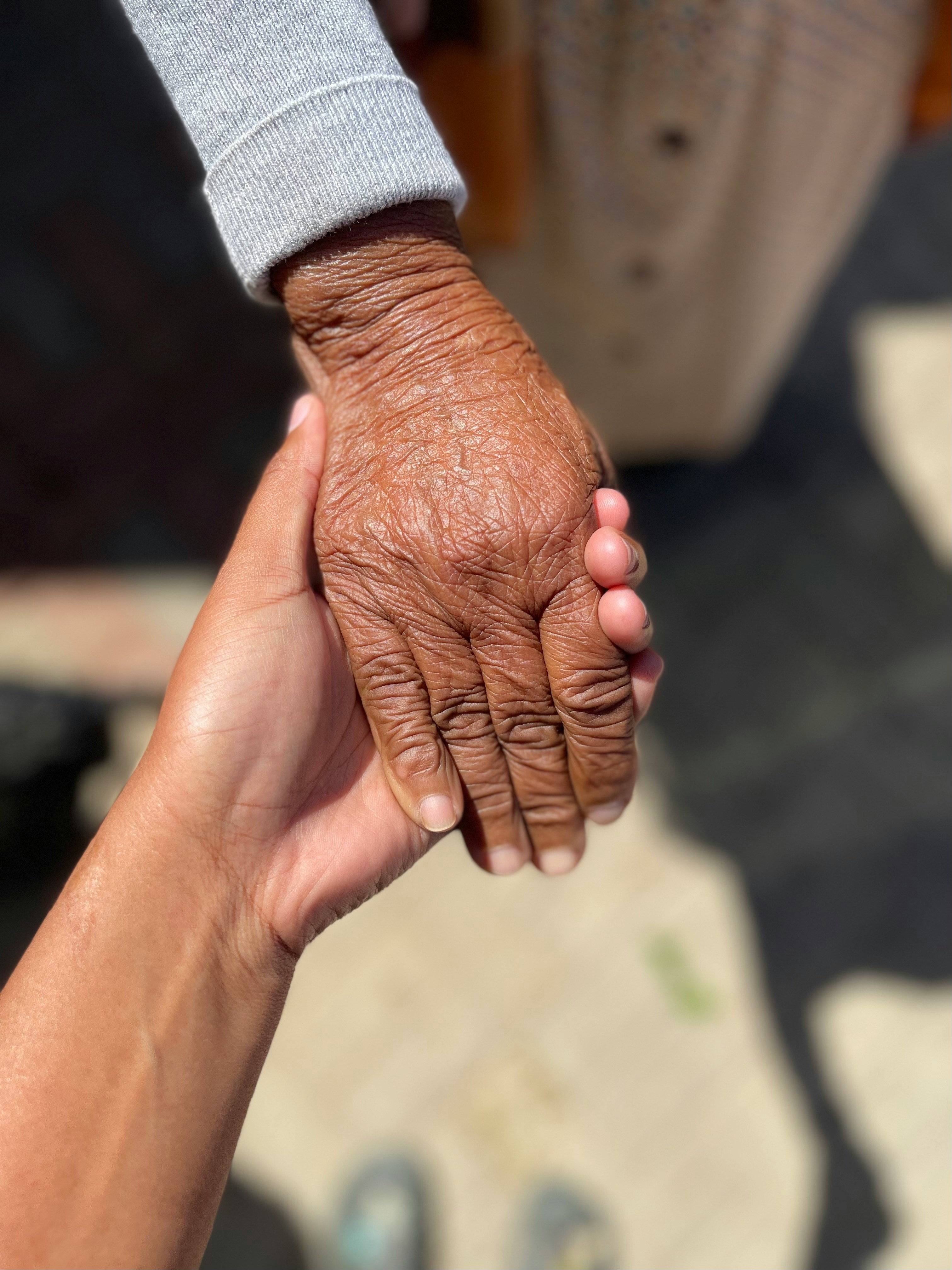 Caregiver holding elderly client's hand in warm sunlight