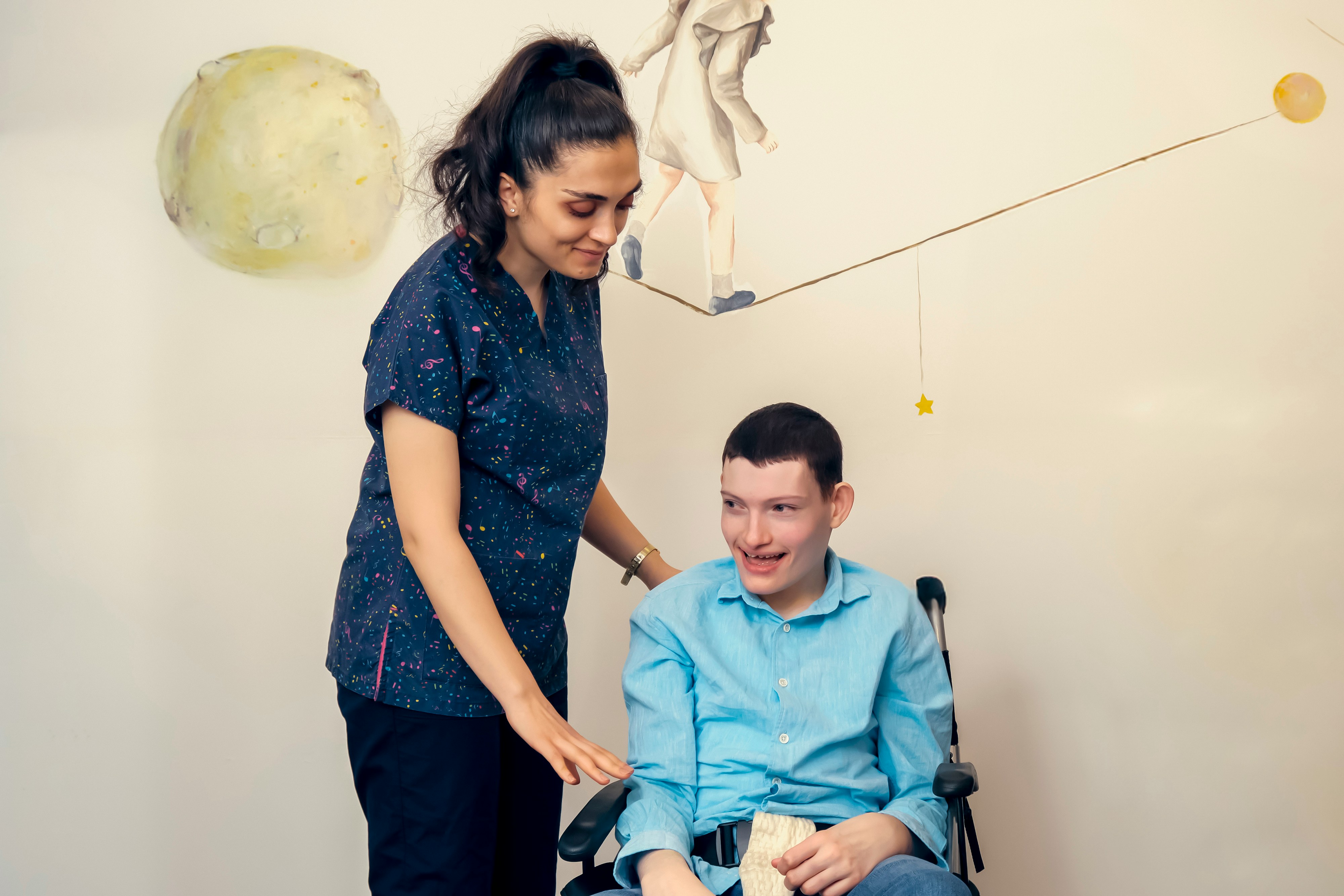 A caregiver smiling warmly with a young person with special needs in a wheelchair, showing compassionate specialized care