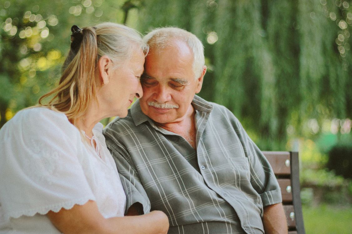 An older couple leaning toward one another on a garden bench
