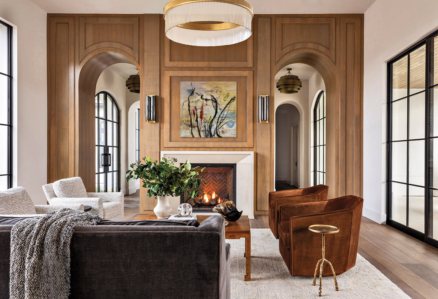 Luxury living room with custom wood millwork, arched doorways, fireplace, designer lighting, and upscale interior finishes.