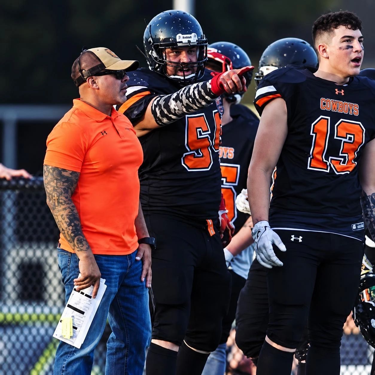 Hector on the sideline in an orange polo beside his players