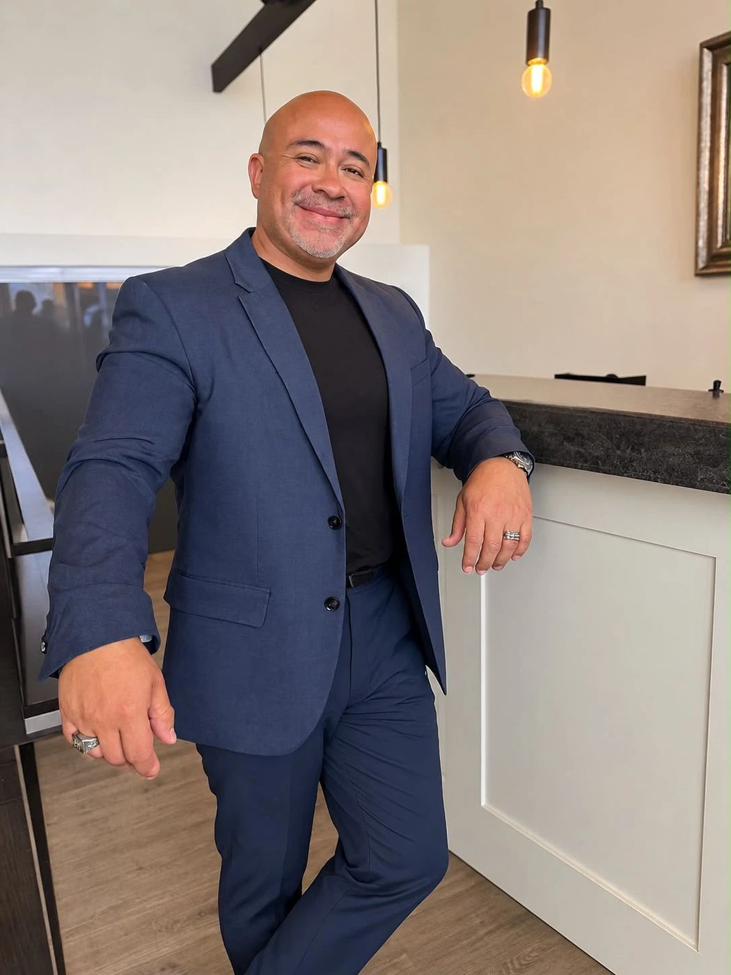 Hector Alvarado in a navy suit, smiling and leaning on a counter