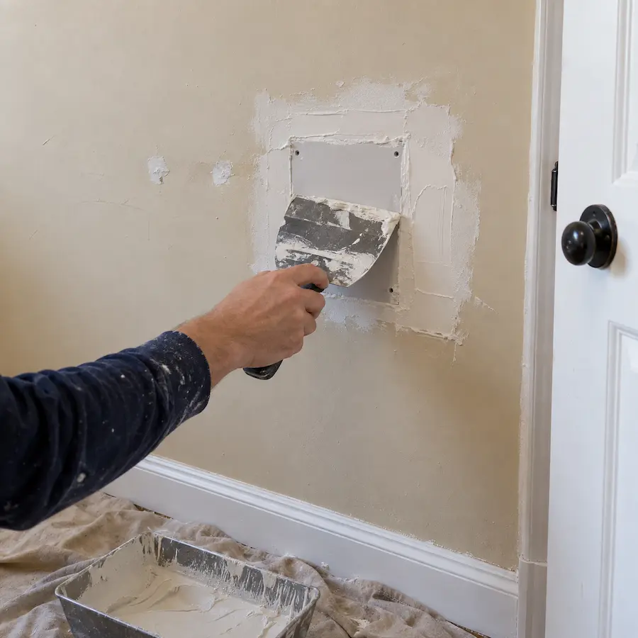 Wet joint compound being spread over a square drywall patch with a taping knife