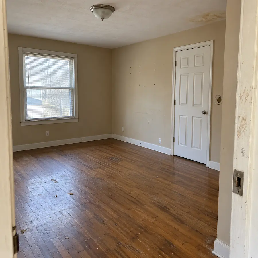 Empty rental bedroom after move-out, with anchor holes, a doorknob hole, scuffed walls, and a ceiling stain