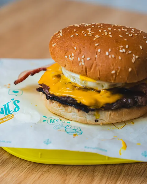 Johnnie's beef burger with bacon, fried egg and melted cheese on a sesame bun in teal-print paper