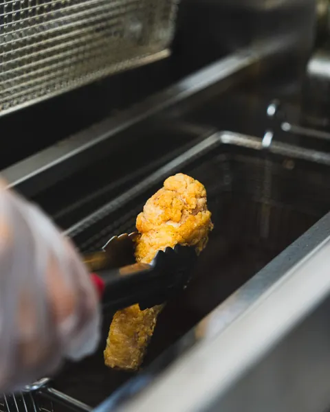 Golden fried chicken lifted fresh from the fryer with tongs in the Johnnie's kitchen