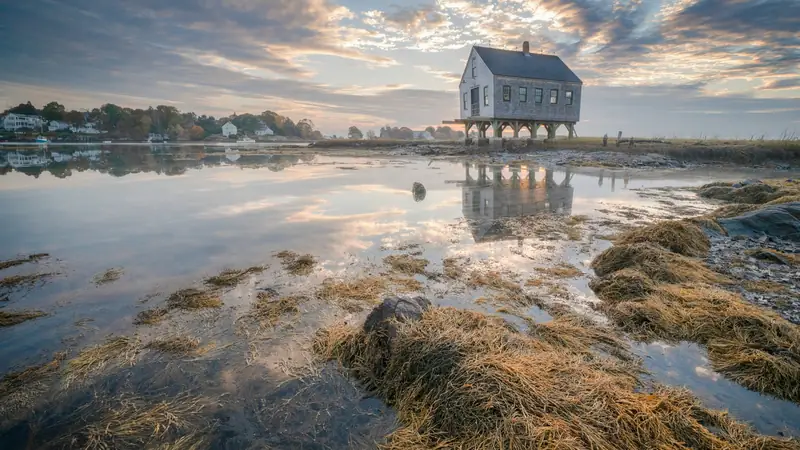 Shingled house raised on pilings above a salt marsh at sunrise
