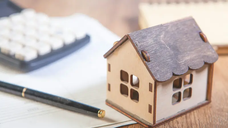 Model house beside a calculator, a pen and paperwork