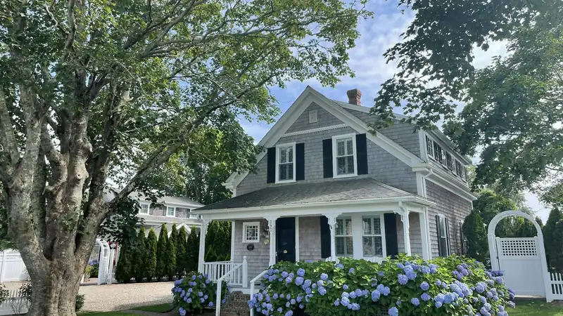 Shingled cape-style house with hydrangeas and a white fence