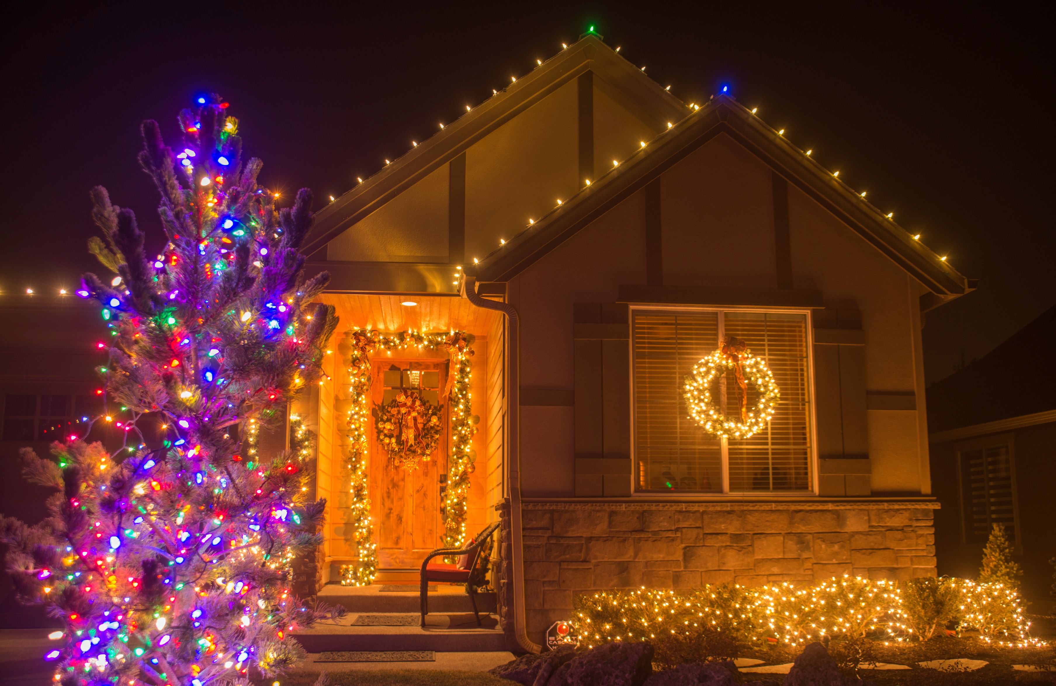 Home with warm white roofline lights, lit wreaths and a multicolor tree