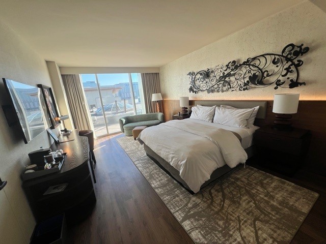 Renovated king guest room at the Westin Nashville featuring a plush white king bed with decorative black wrought-iron floral wall art, hardwood floors, floor-to-ceiling windows with city views, a wall-mounted flat-screen TV, and a teal accent chair