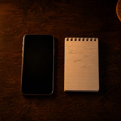 A phone face down beside a spiral notepad on a dark desk.