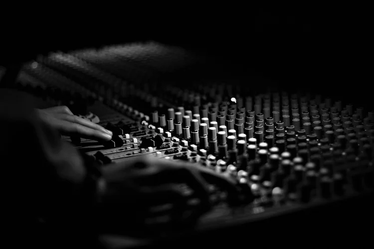 Black and white close-up of hands adjusting a professional mixing console