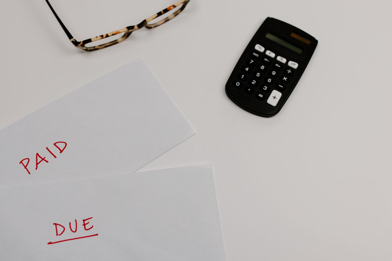 Two sheets of paper labeled PAID and DUE next to a calculator and reading glasses
