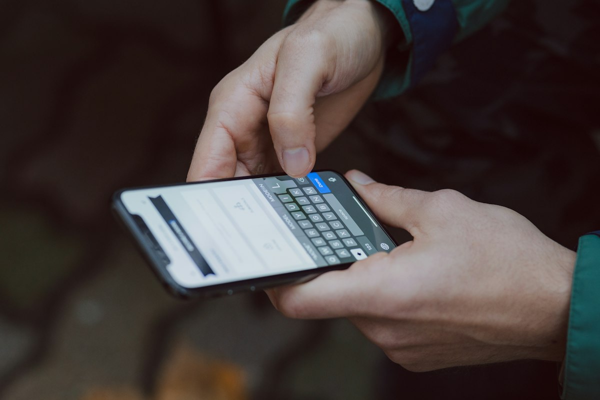A person typing a message on a smartphone, representing a tenant sending a maintenance request after hours