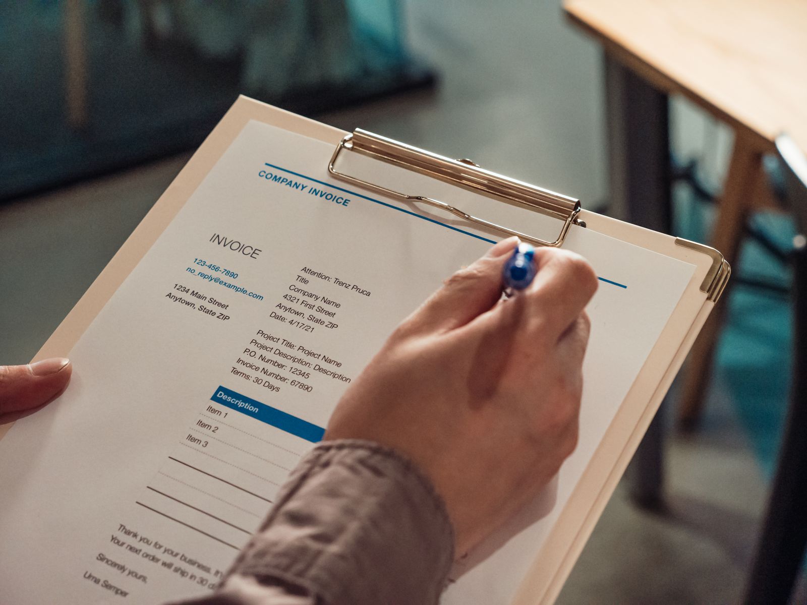 A person filling out a company invoice on a clipboard with a blue pen