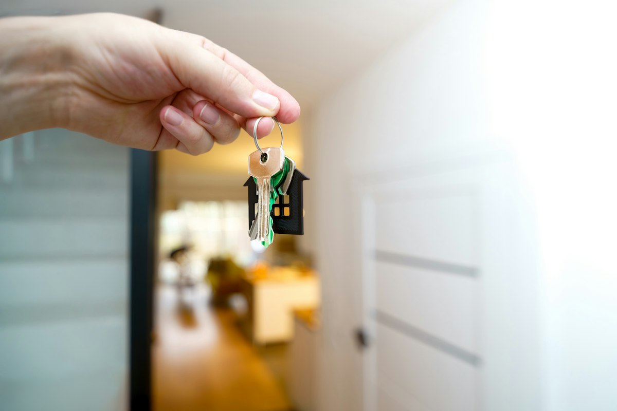 A hand holding a set of house keys with a house-shaped keychain inside a bright apartment entrance, symbolizing a lease renewal