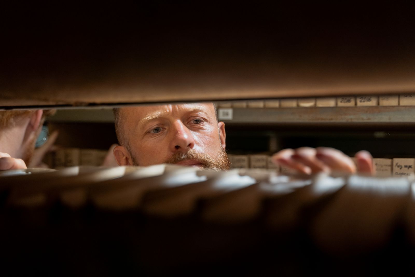 A man searching carefully through labeled archive boxes on a shelf, representing a search through old customer records