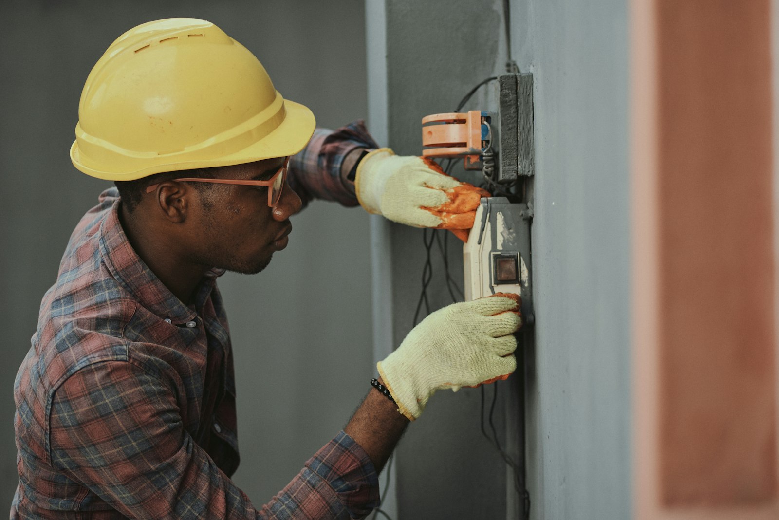An electrician in a yellow hard hat and work gloves installing wiring on a wall, representing the skilled trades labour shortage