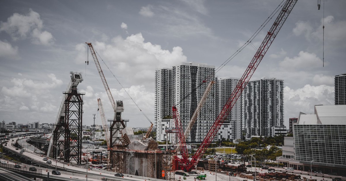 Construction cranes and a half-built bridge tower beside high-rise buildings under a cloudy sky, representing Ontario's shifting construction work in 2026