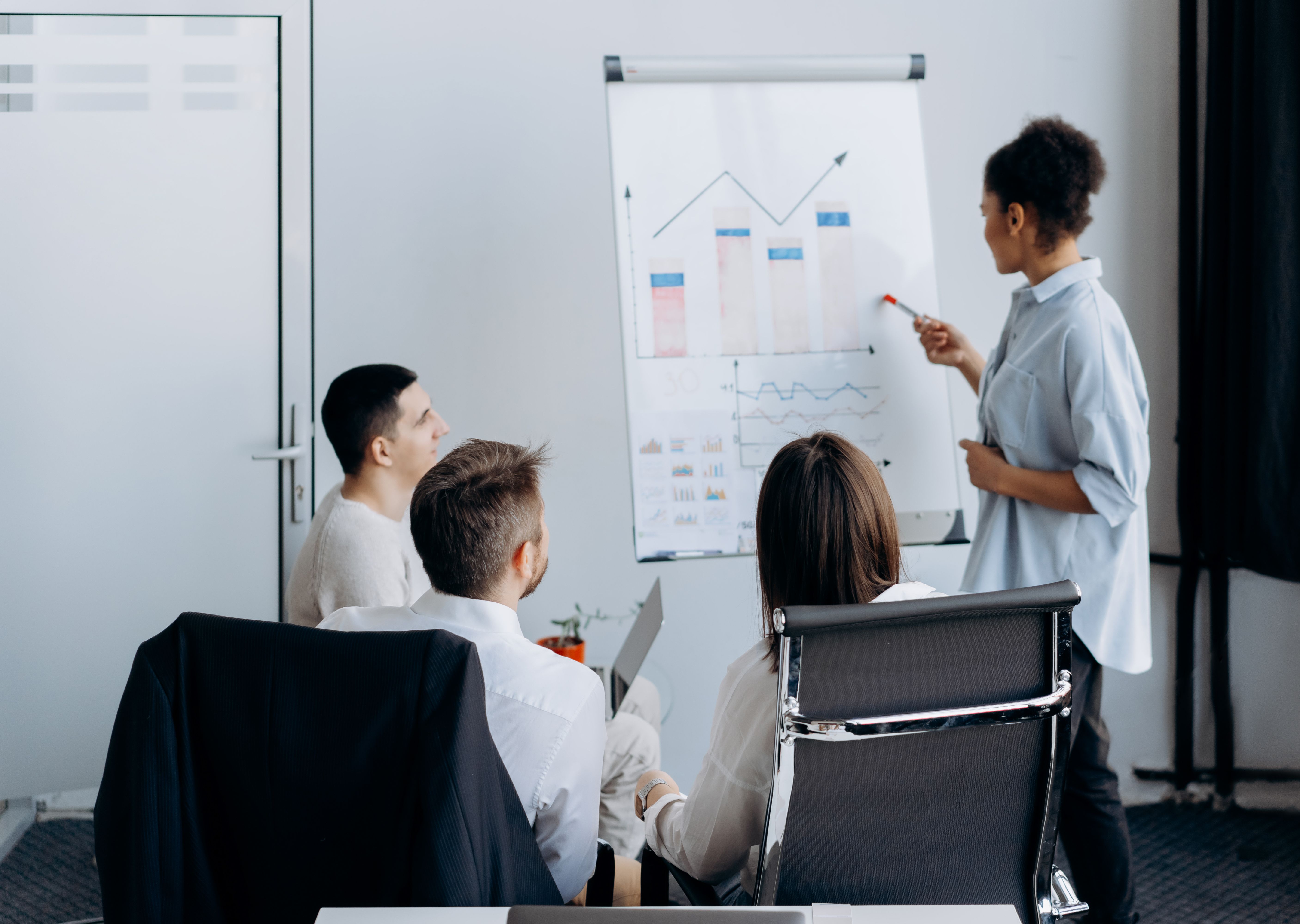 A manager presents to a small team of employees in an office setting, explaining how to use a new AI tool with real workflow examples rather than generic feature overviews