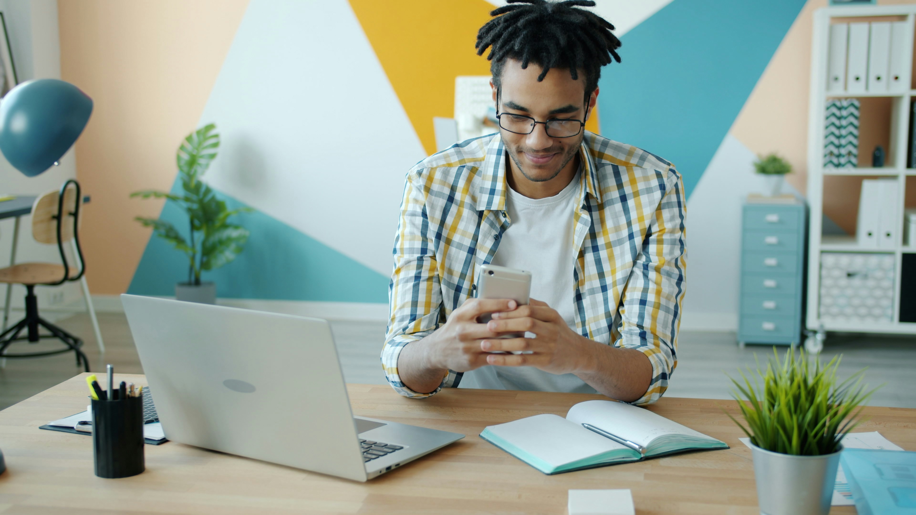 A professional quietly checks a smartphone at their desk beside a laptop, representing an employee using a personal AI tool without company approval