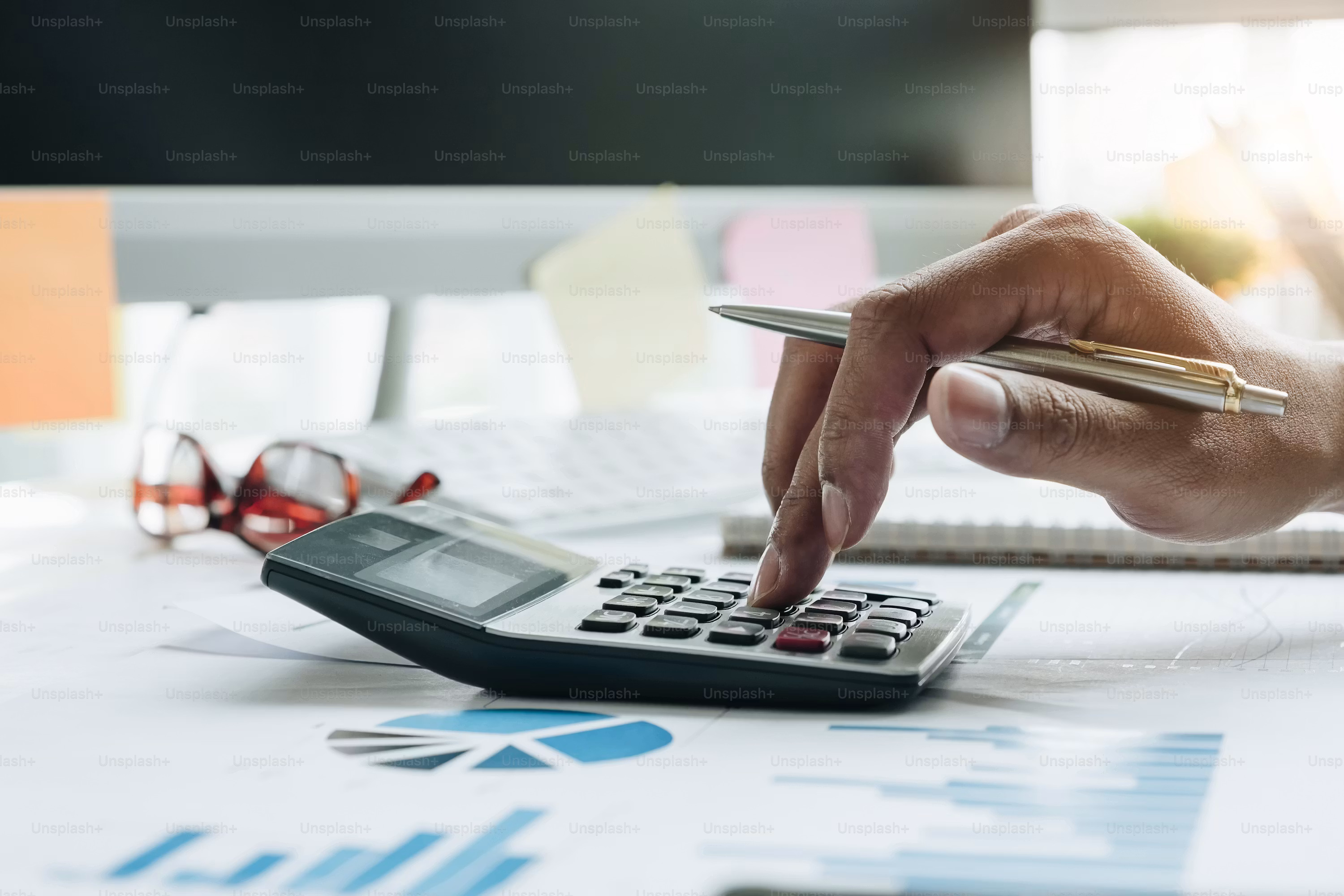 A bookkeeper works through business documents with a calculator and laptop, representing the manual spreadsheet process AI cash flow forecasting replaces