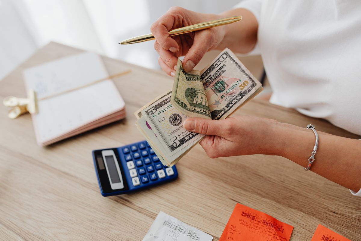 A small business owner counts U.S. dollar bills next to a calculator and receipts on a desk, representing the cost pressure squeezing profit margins